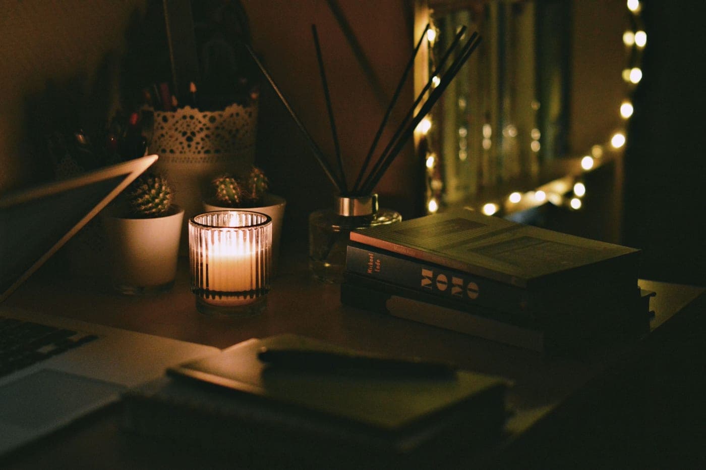 A laptop and notebook on a desk lit by a single lamp
