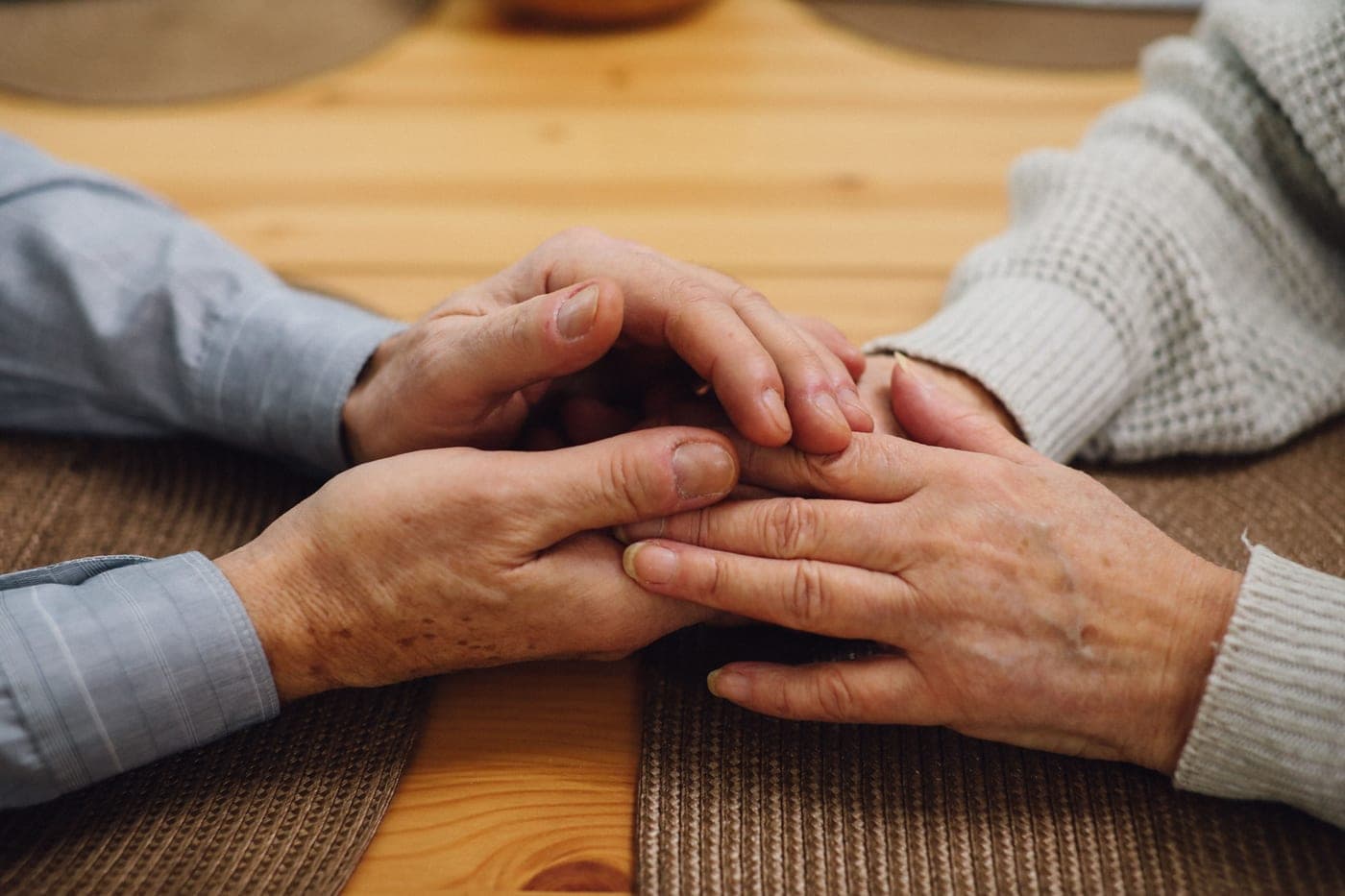 A close-up of an elderly couple's hands resting together on a wooden table