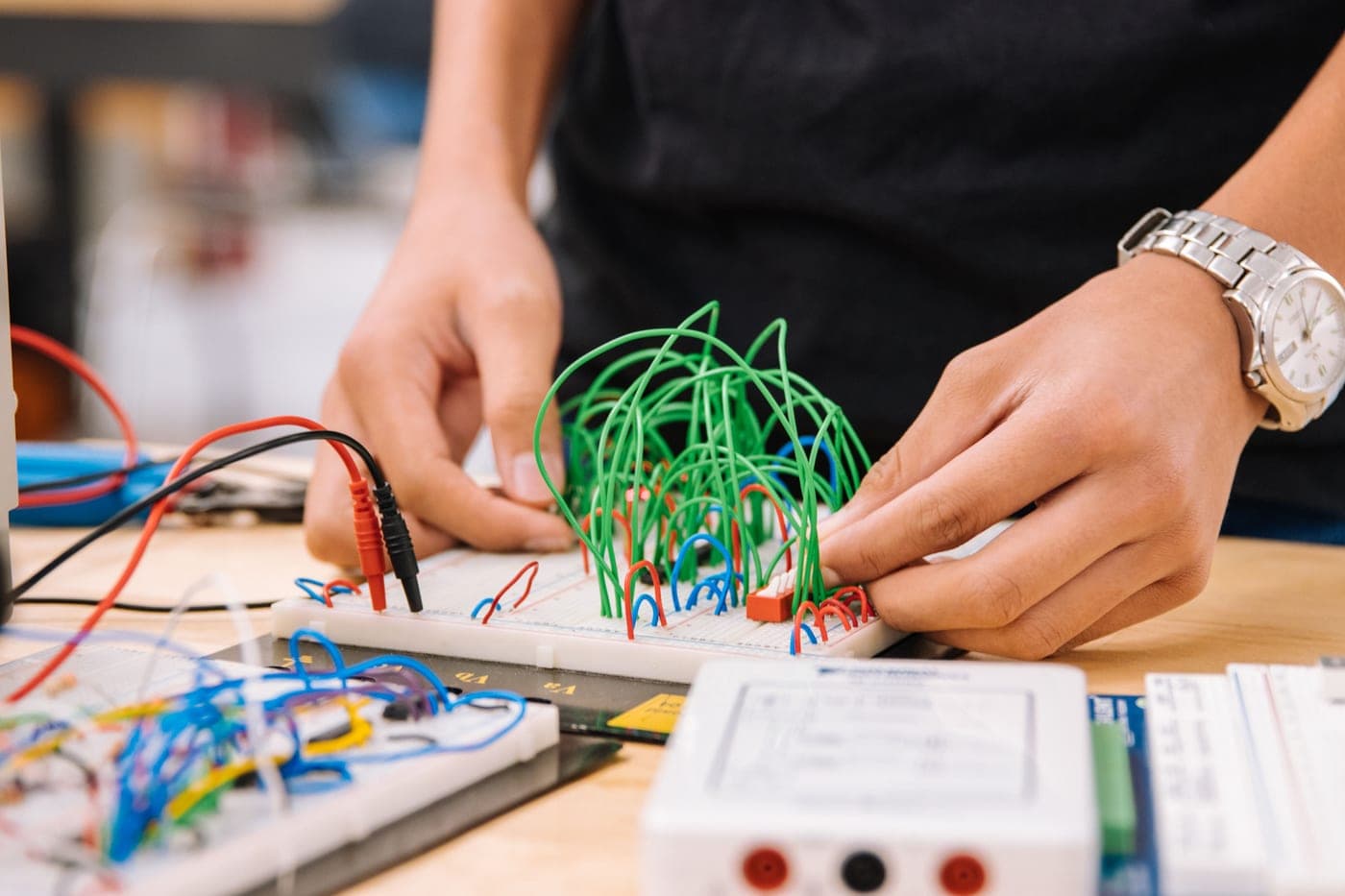 Hands working with colored wires on an electronics breadboard