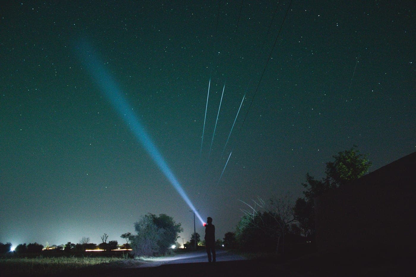 A person shining a flashlight upward at a star-filled night sky