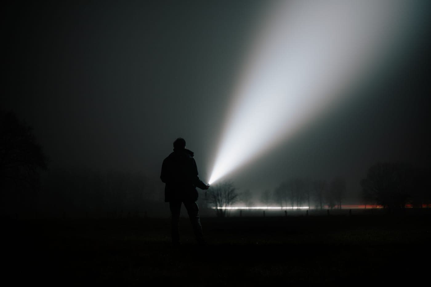 A person holding a flashlight in a foggy night landscape