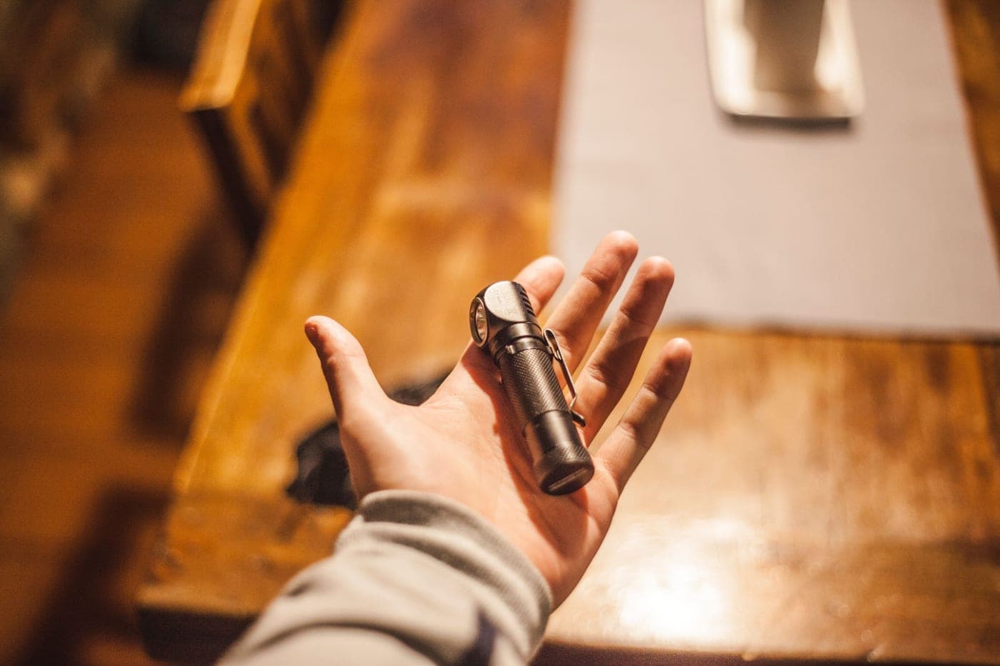 A hand holding a flashlight on a wooden table in warm indoor light