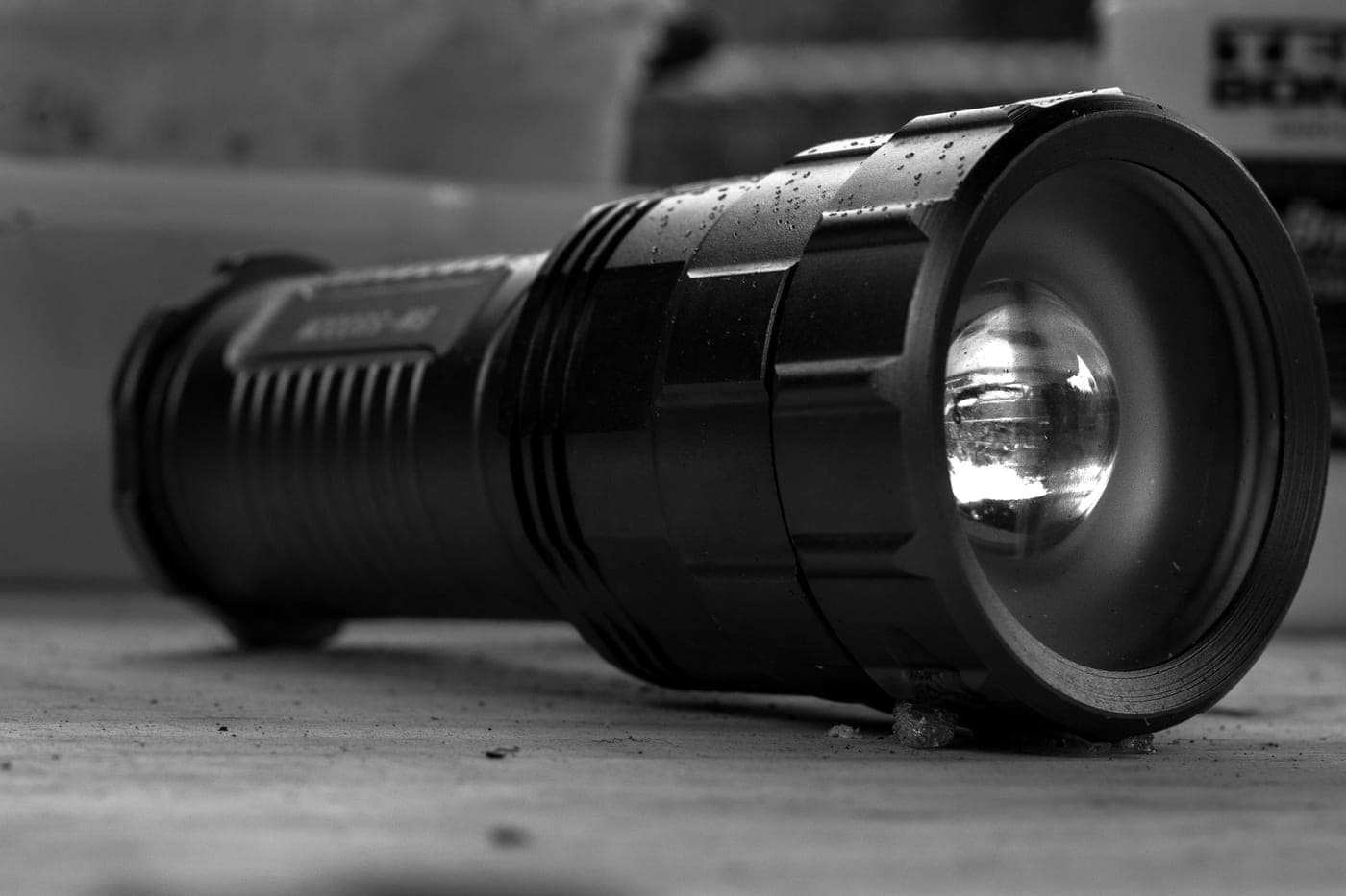 A black metal flashlight lying on a dusty surface, photographed close up