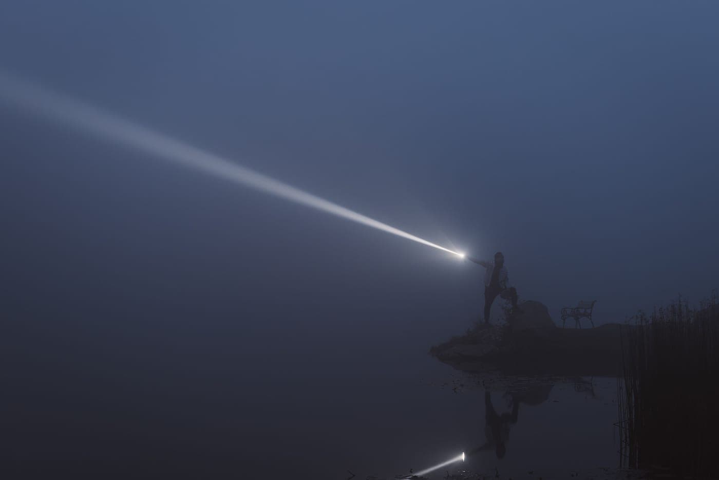 A flashlight beam lighting mist over a lake at night