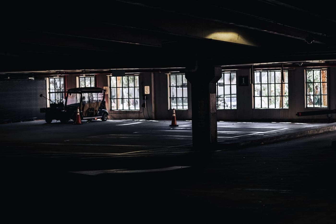 A dark, empty parking garage dimly lit, with a vehicle silhouetted