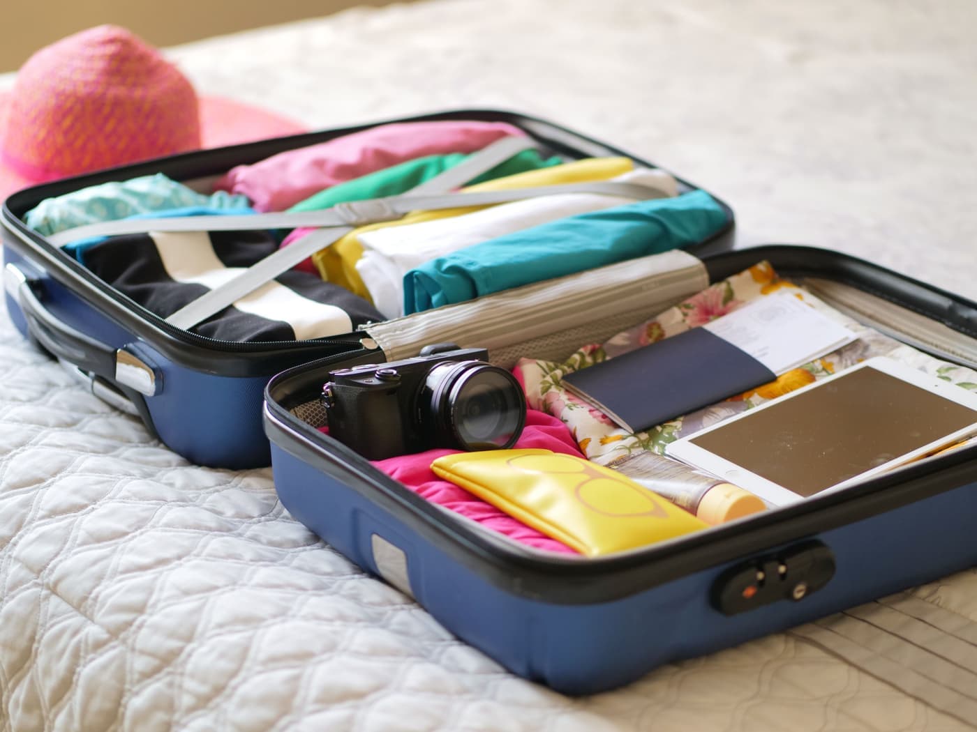 An open suitcase packed with clothes, a camera and a passport