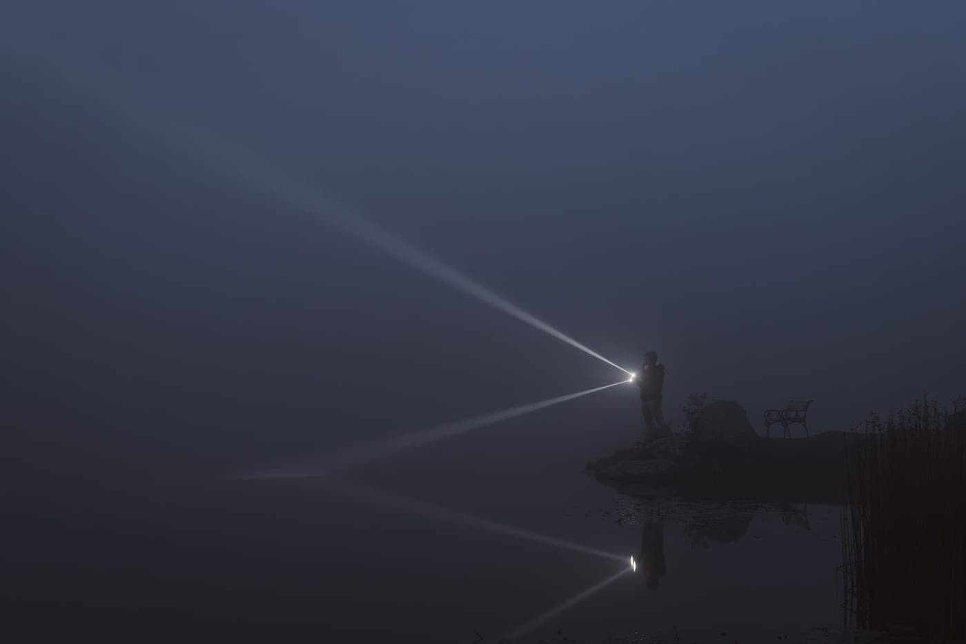 A person lighting a foggy lakeside at night with a handheld light