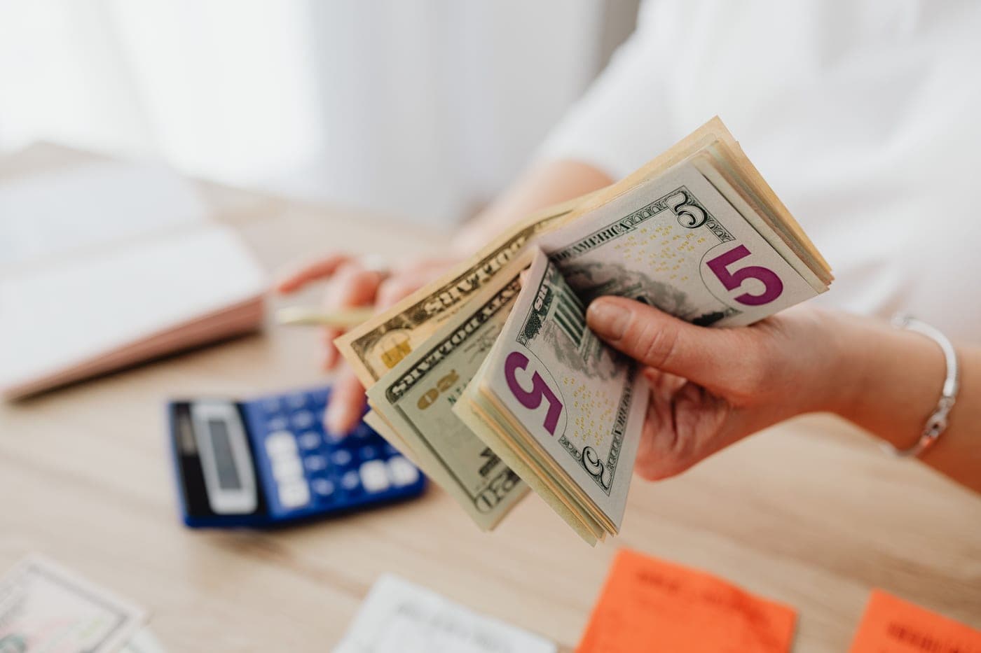 A hand holding banknotes beside a calculator