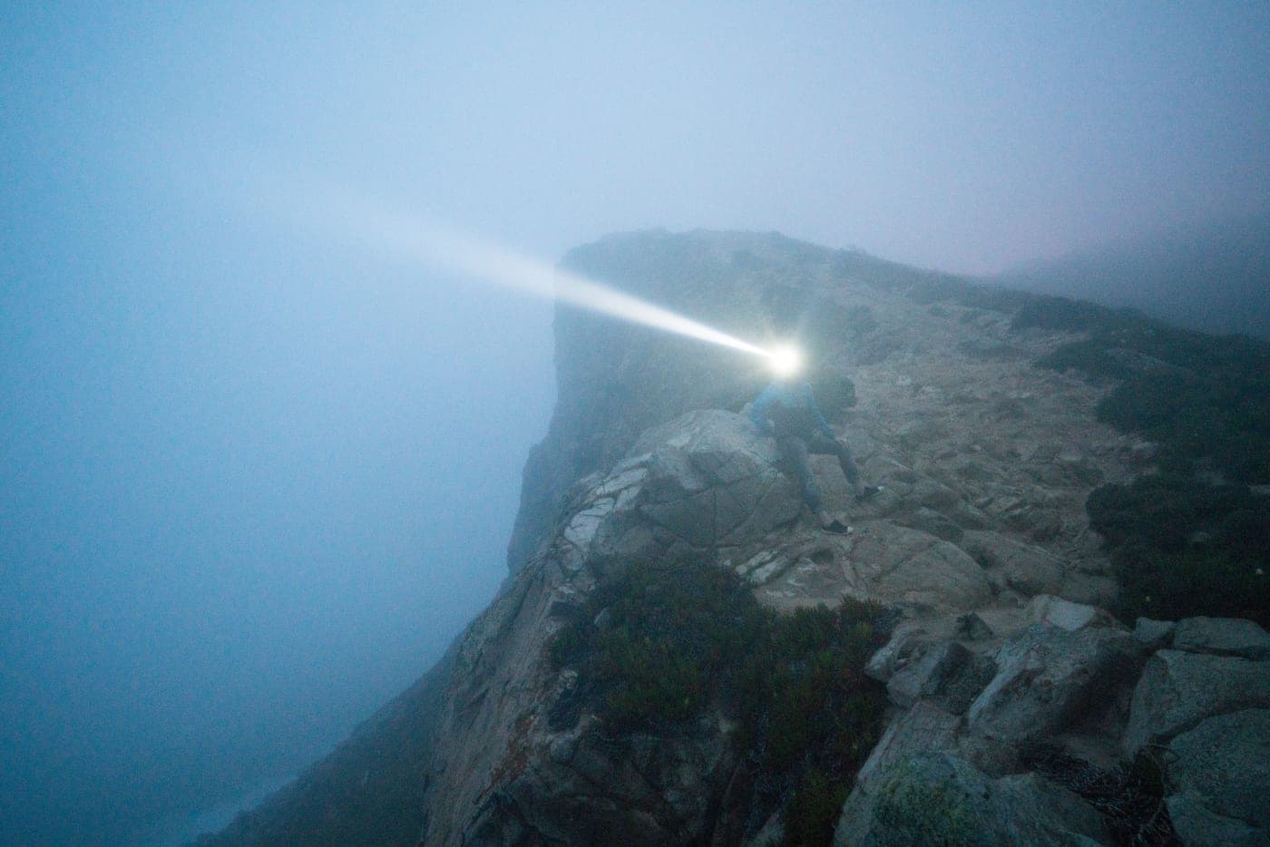 A person with a bright light sitting on a rocky cliff top on a foggy night