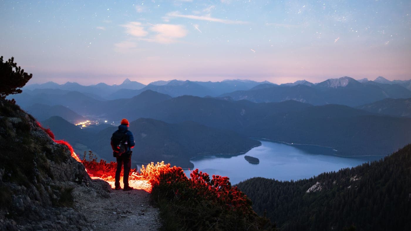 A hiker with a backpack looking over a lake at dusk
