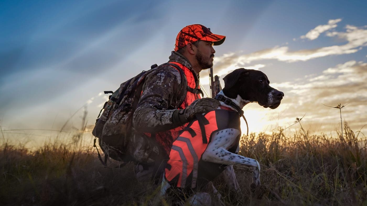 A hunter walking through an open field at first light