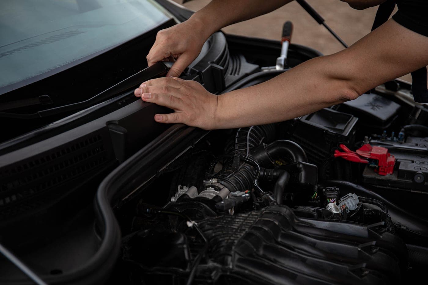 Close-up of a mechanic hands working on a car windshield wiper and engine components