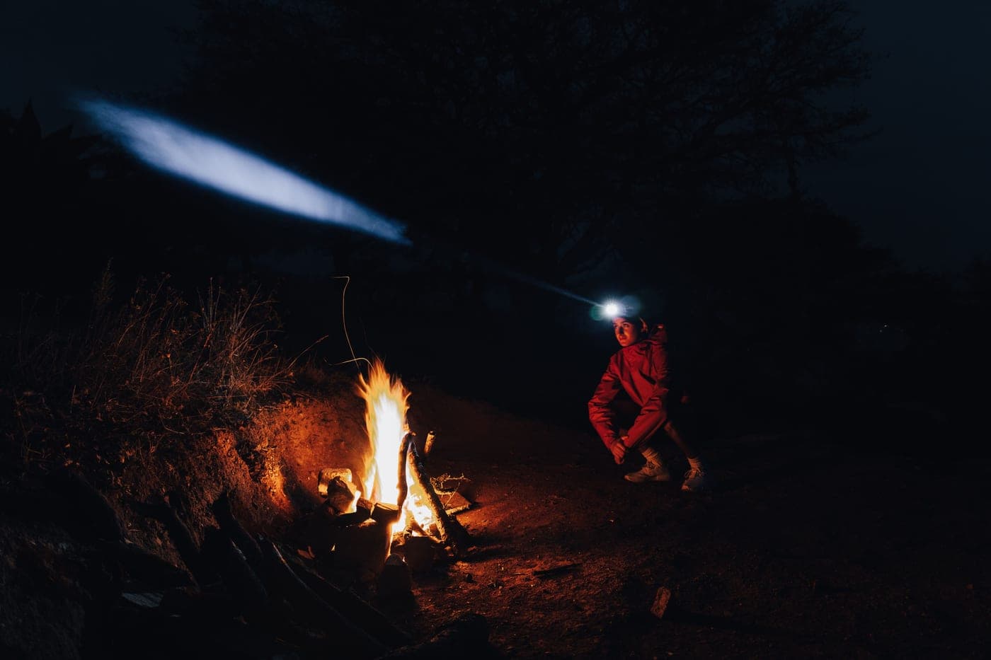 A person wearing a headlamp sitting by a campfire at night