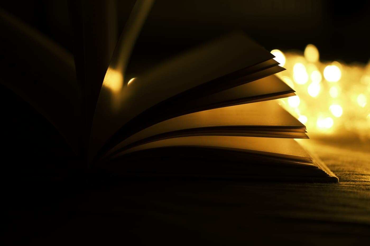 An open book beside warm fairy lights in a dim room