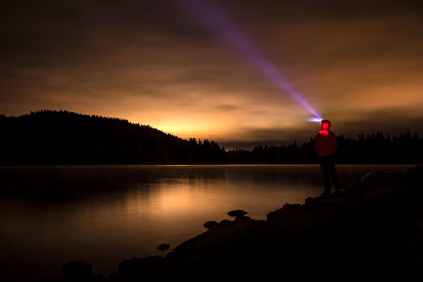 A hiker wearing a headlamp on a dark trail at night