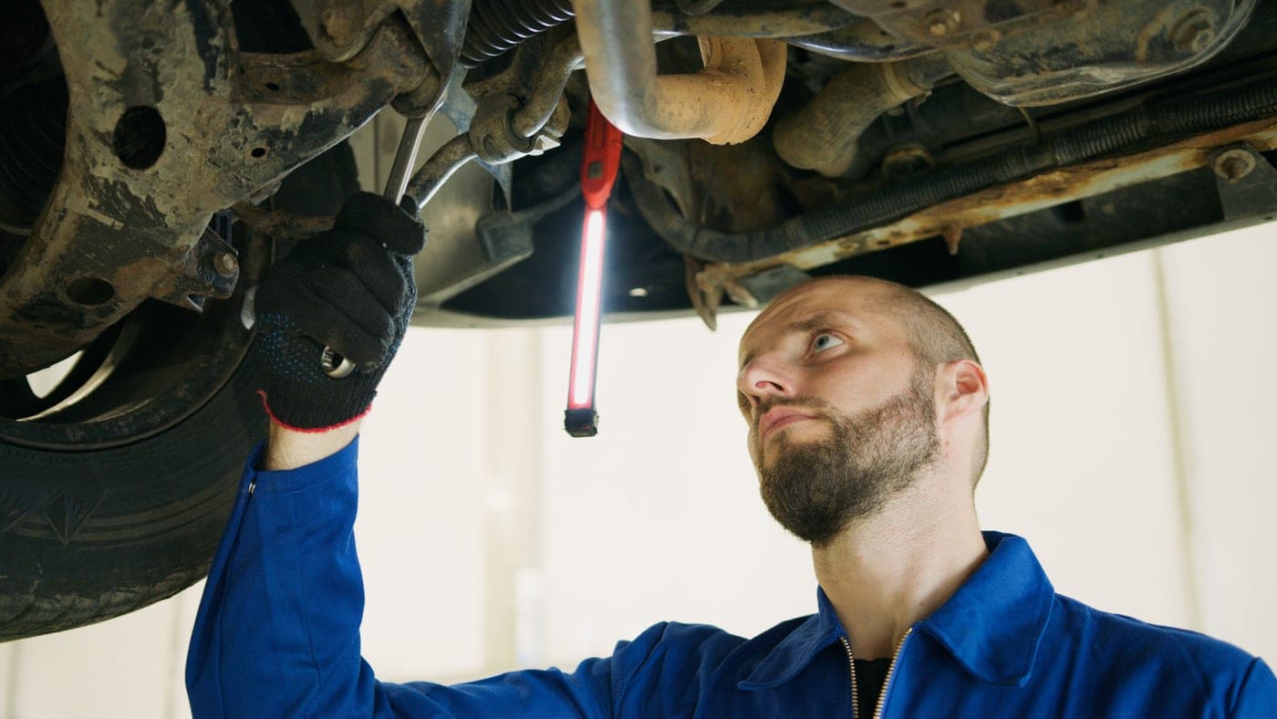 A mechanic working beneath a vehicle lit by a portable work light