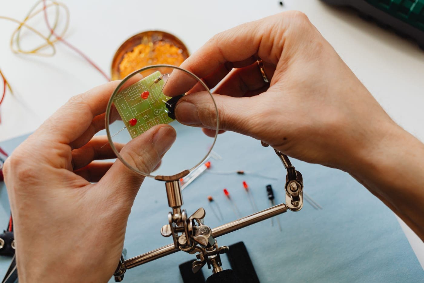 A close-up of hands working on a circuit board under a magnifier