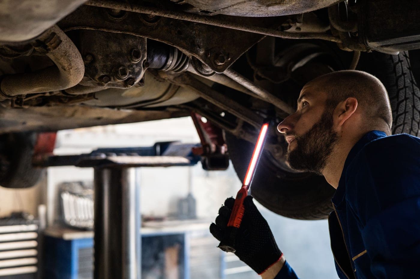 A mechanic using a light to inspect a vehicle undercarriage in a workshop